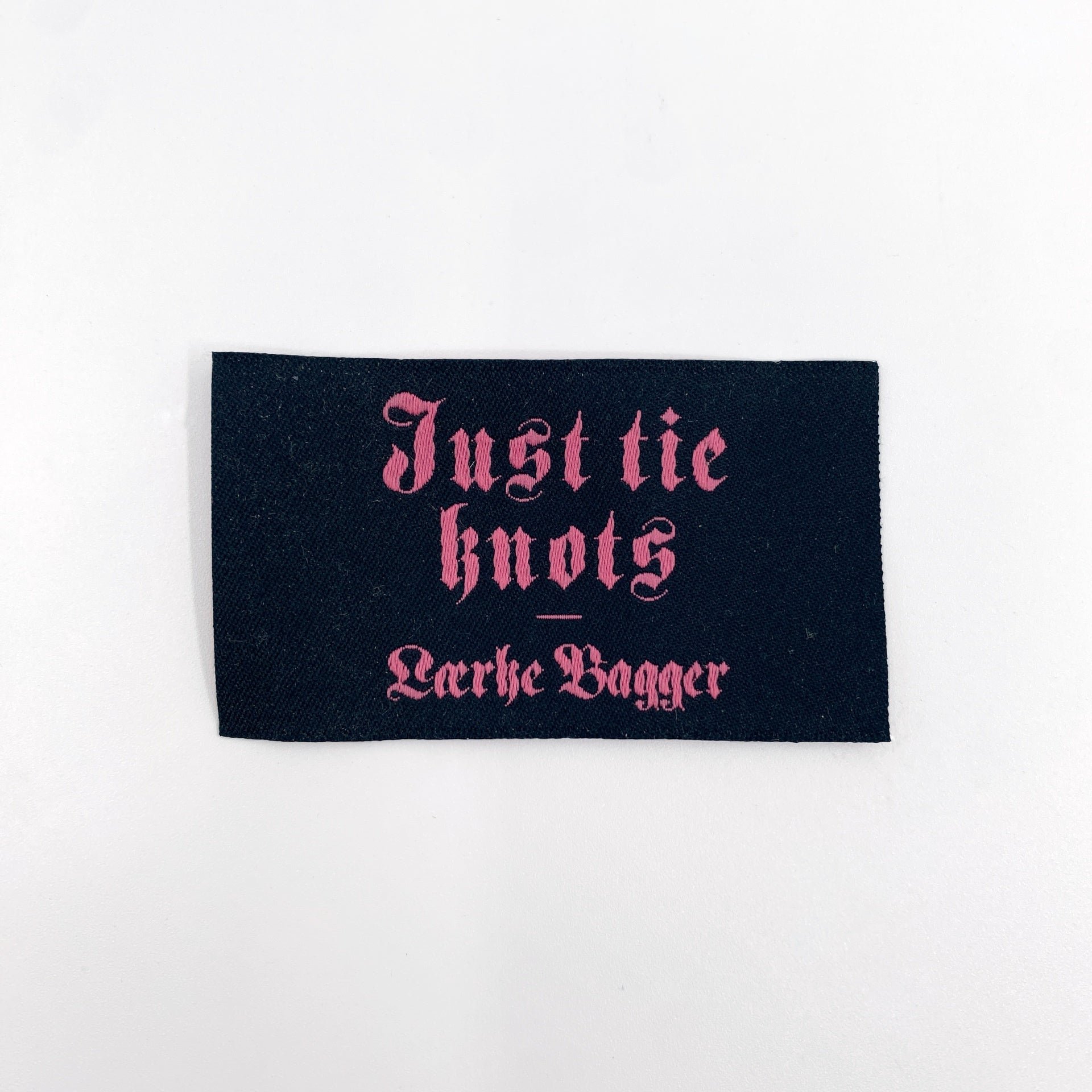 Sort label med rosa tekst med teksten just tie knots Lærke Bagger